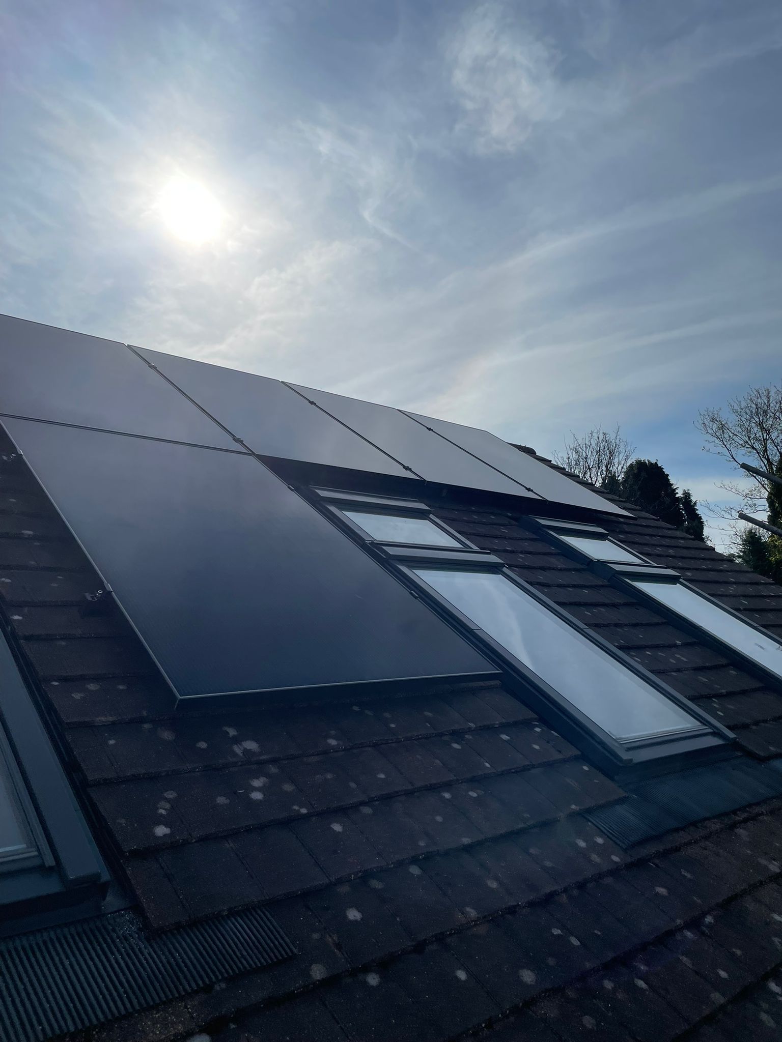 Solar panels installed on a tiled roof with skylights, under a sunny sky.