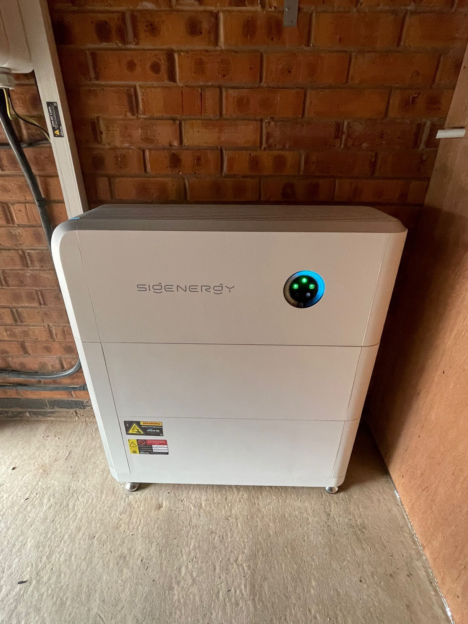 White energy storage unit with a blue light against a brick wall.