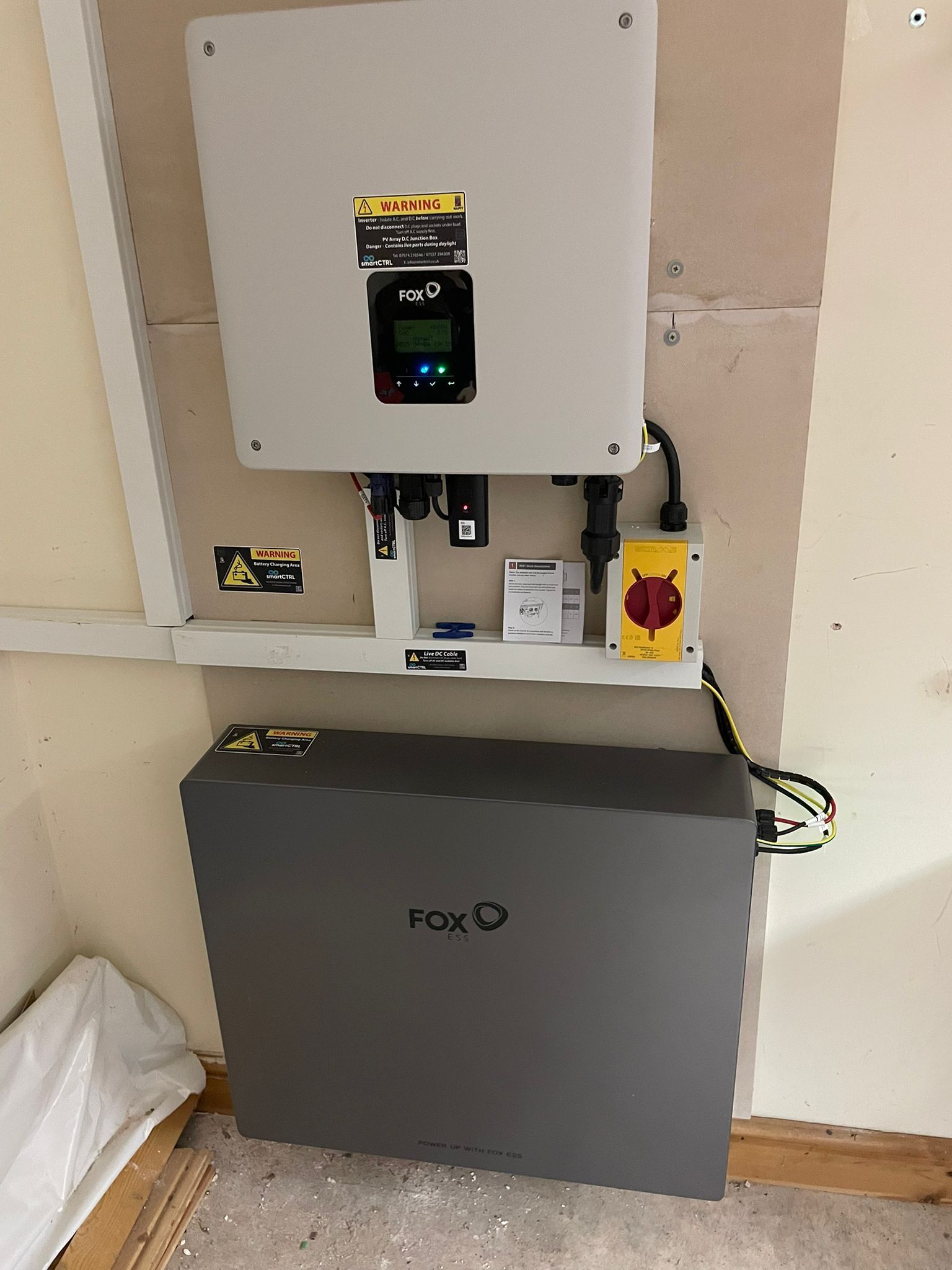 Solar power system: inverter and battery mounted on a wall. Gray and white components with various cables and controls.