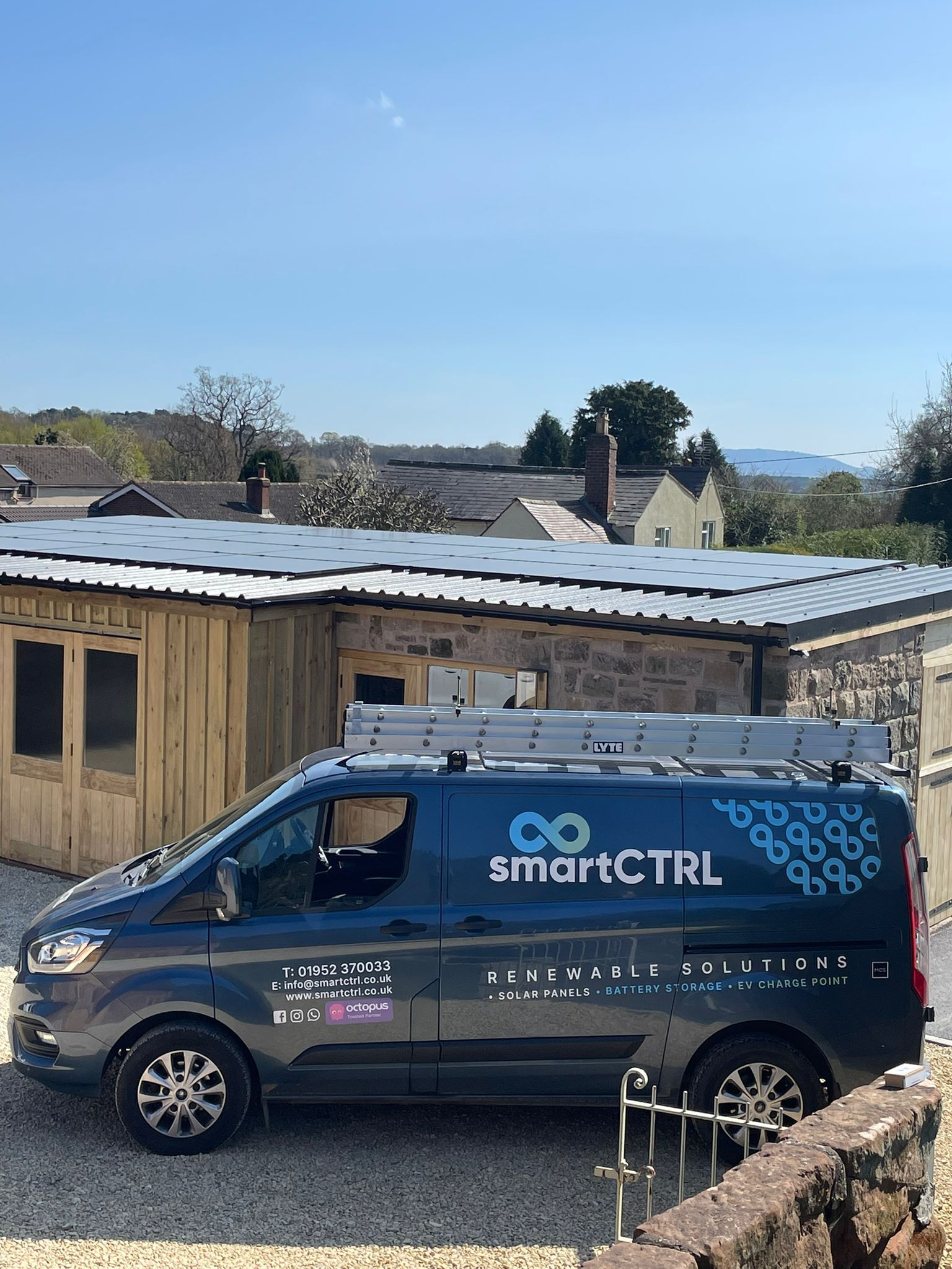 Dark blue SmartCTRL van parked in front of a shed, under a blue sky, ladders on top.