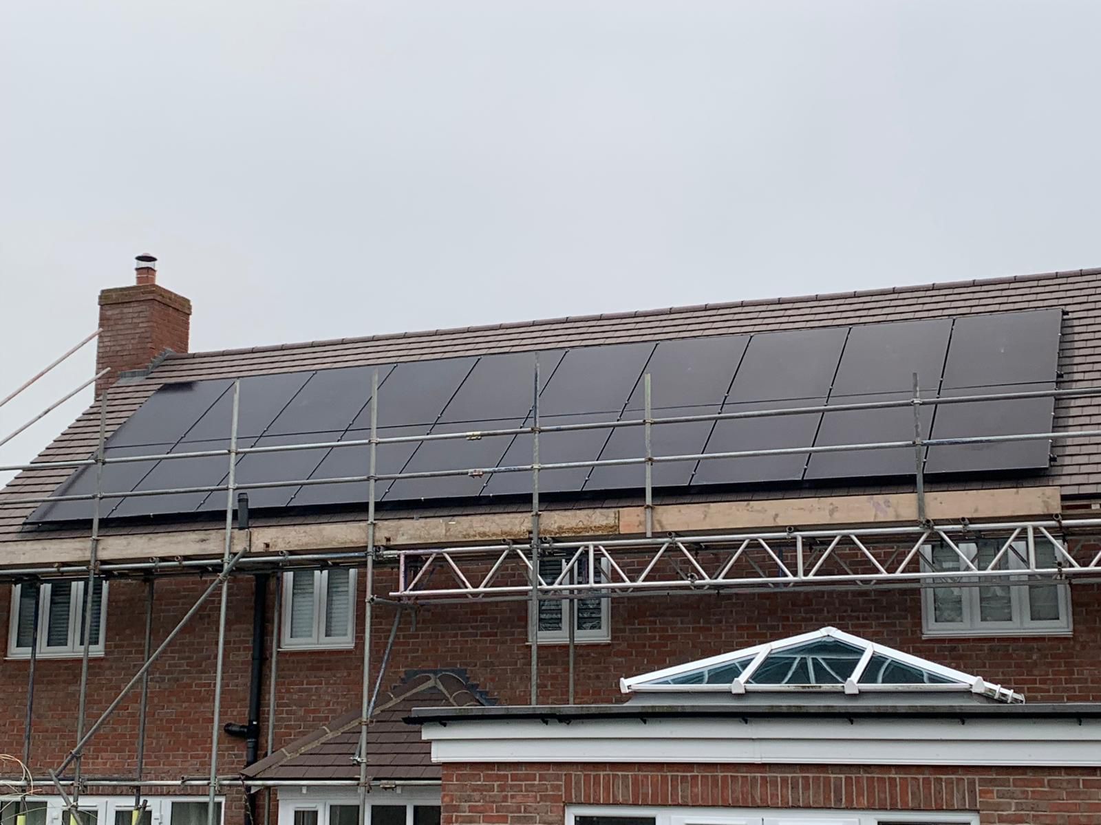 Solar panels installed on a brick house roof with scaffolding. Overcast day.