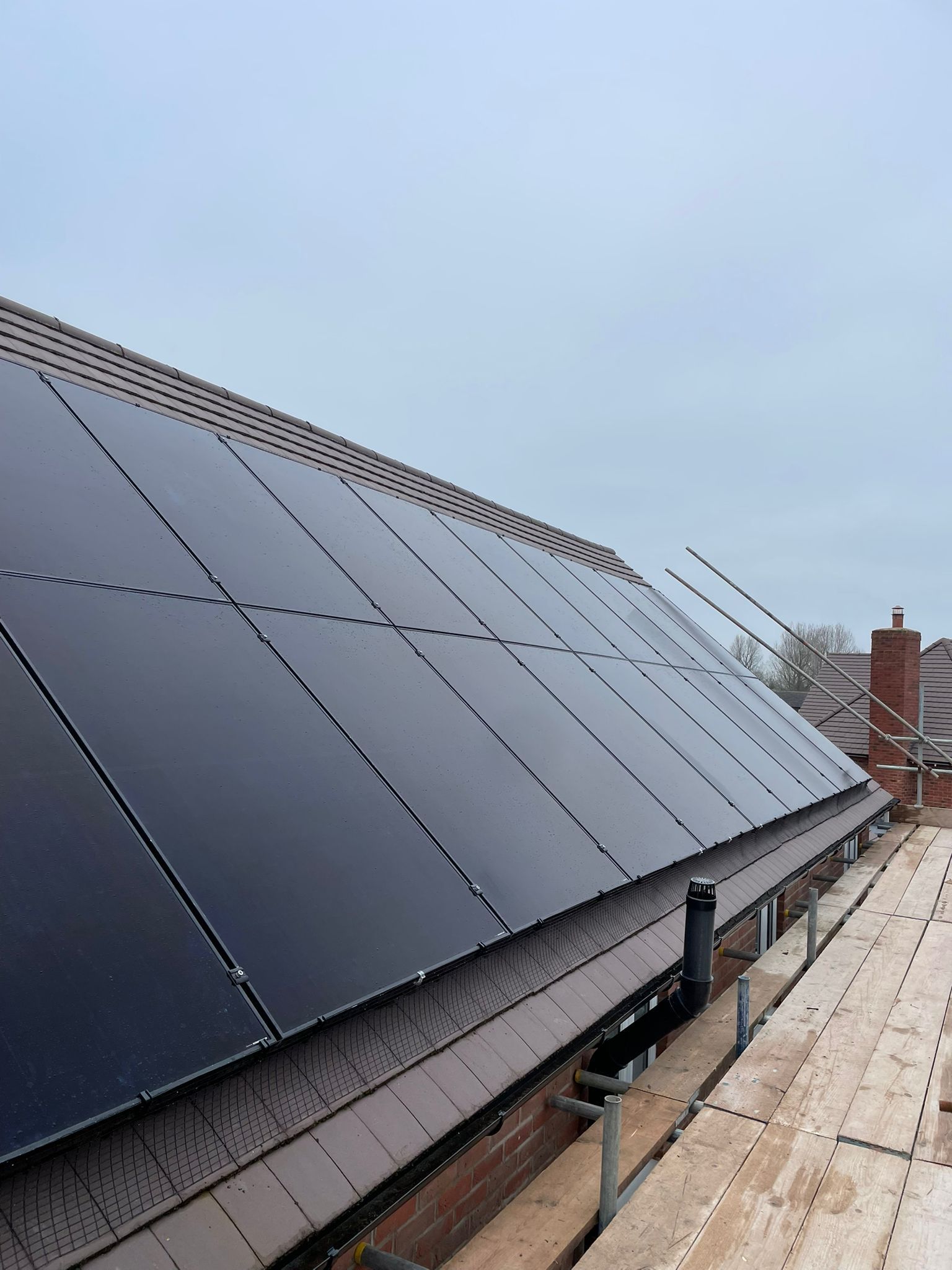 Solar panels on a sloped roof. Grey sky, scaffolding, and chimney visible.