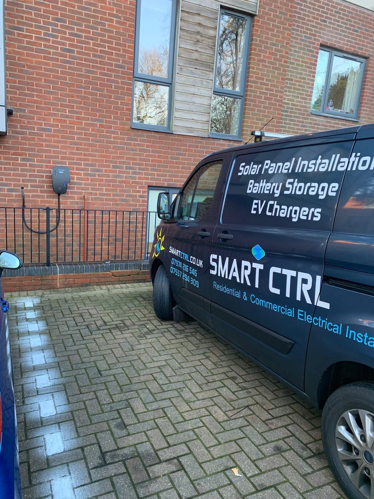 Van parked in front of a brick building next to an EV charger. The van is labeled