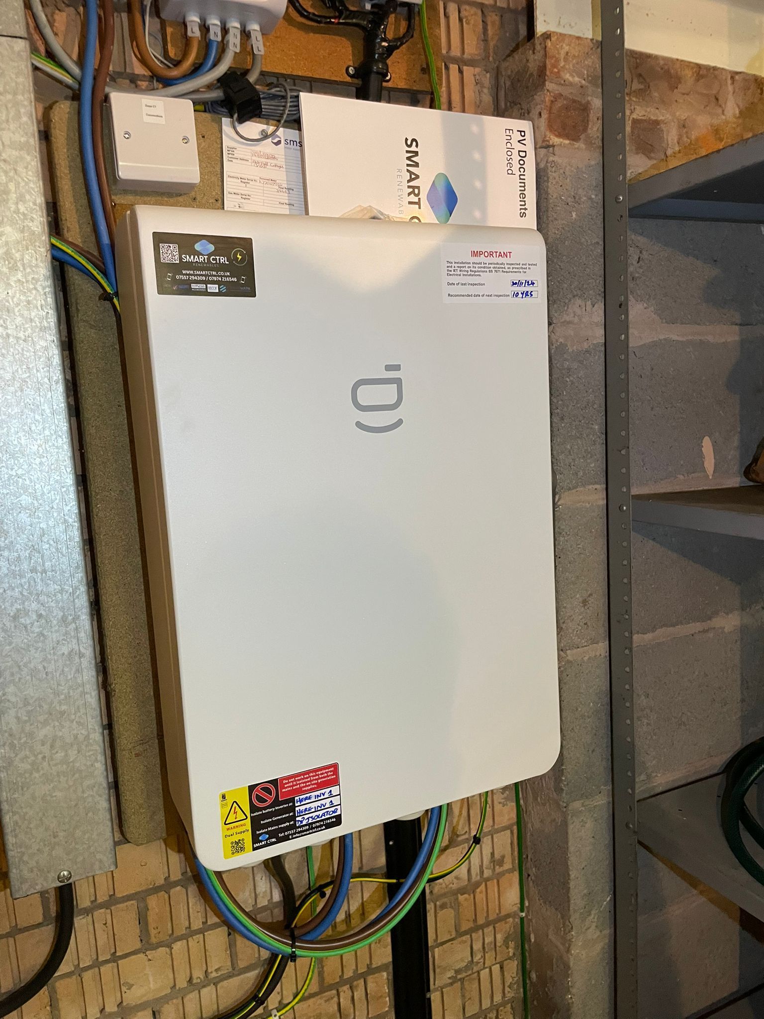 White electrical panel mounted on a brick wall with wires.