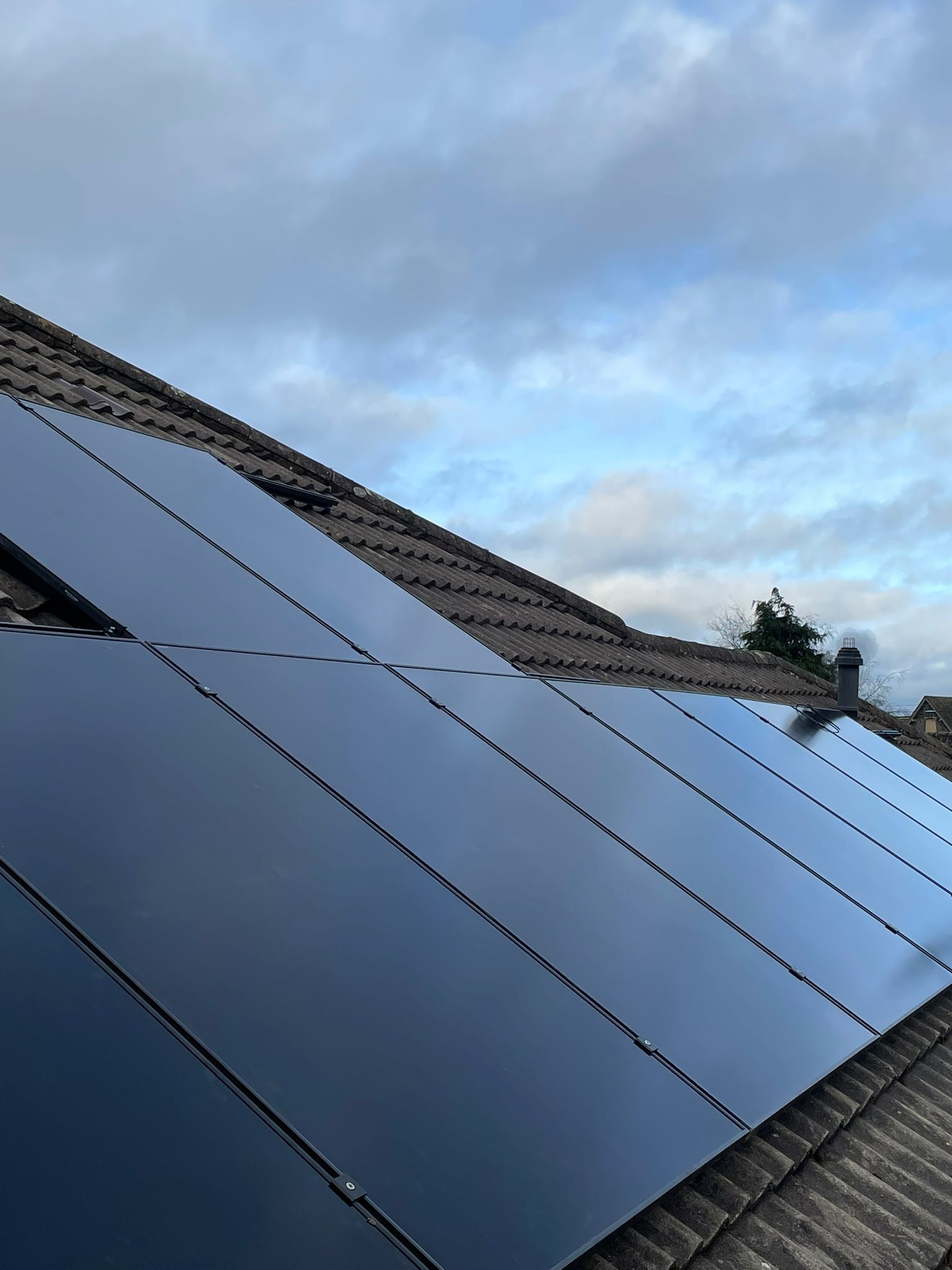 Solar panels installed on a dark tiled roof against a cloudy sky.