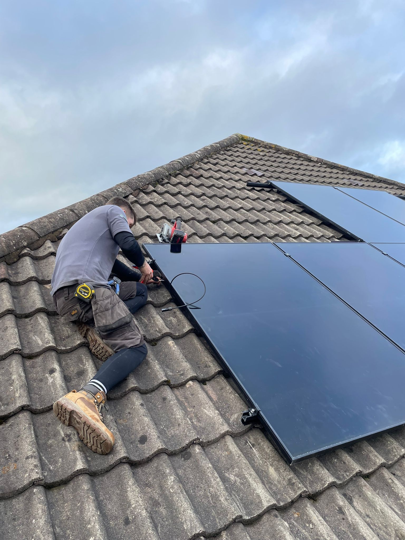 Person installing solar panels on a rooftop. The person is using a drill.