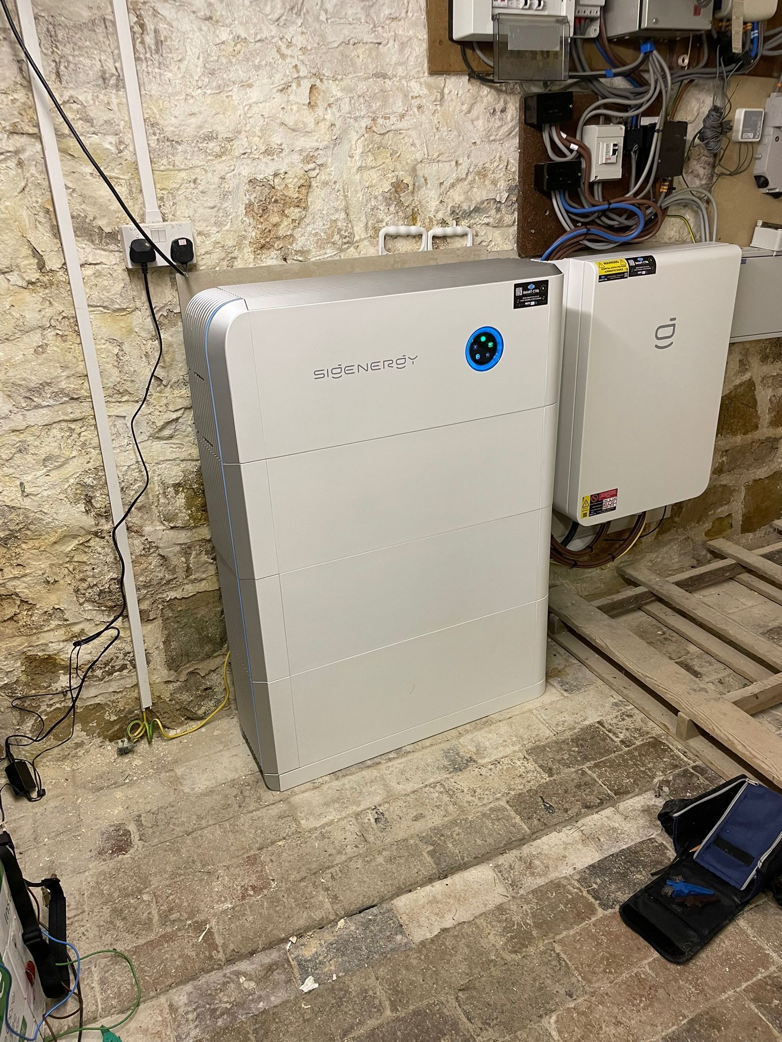 A white energy storage system and an attached white box mounted on a stone wall.