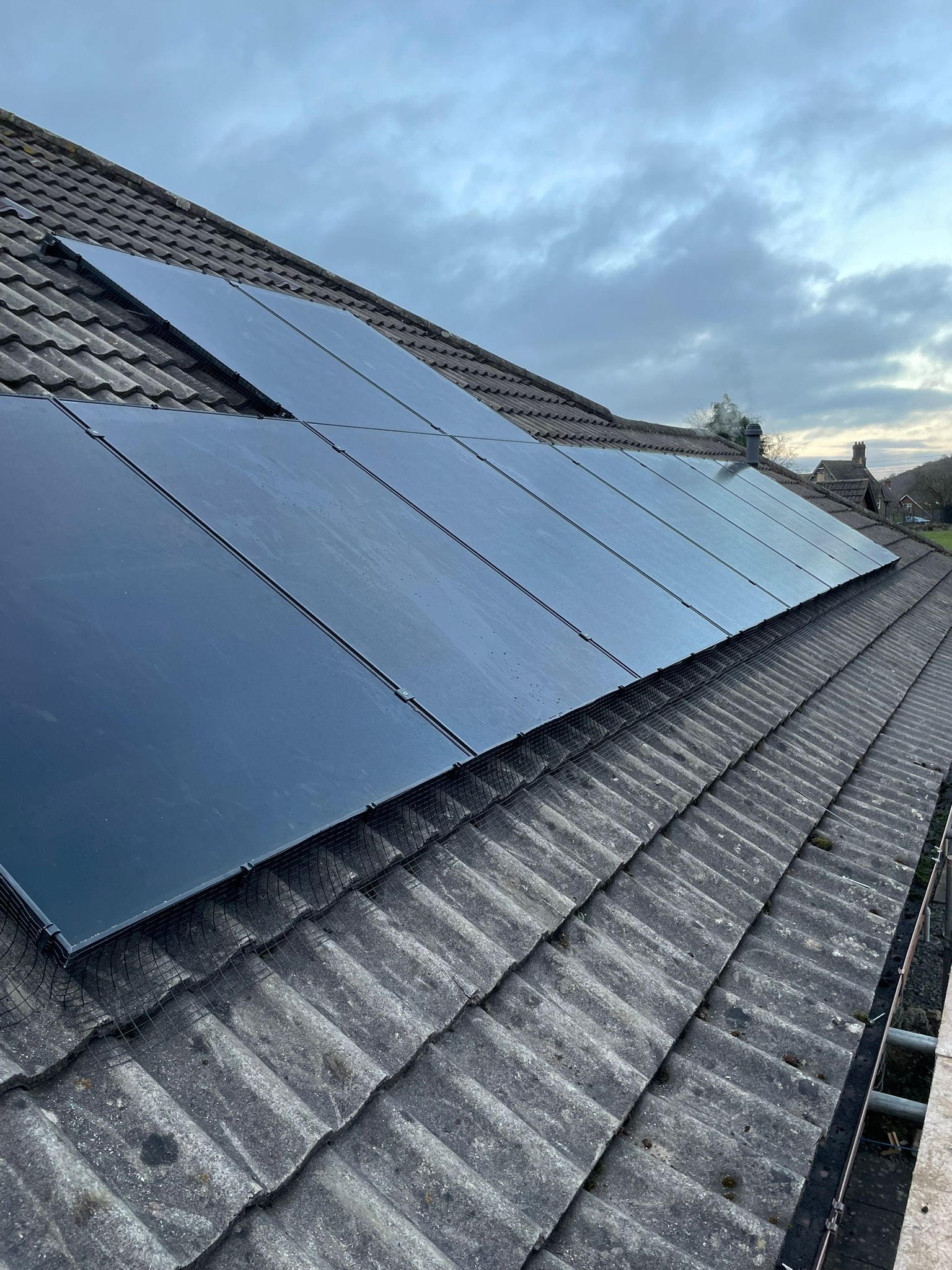 Solar panels installed on a tiled roof under a cloudy sky.