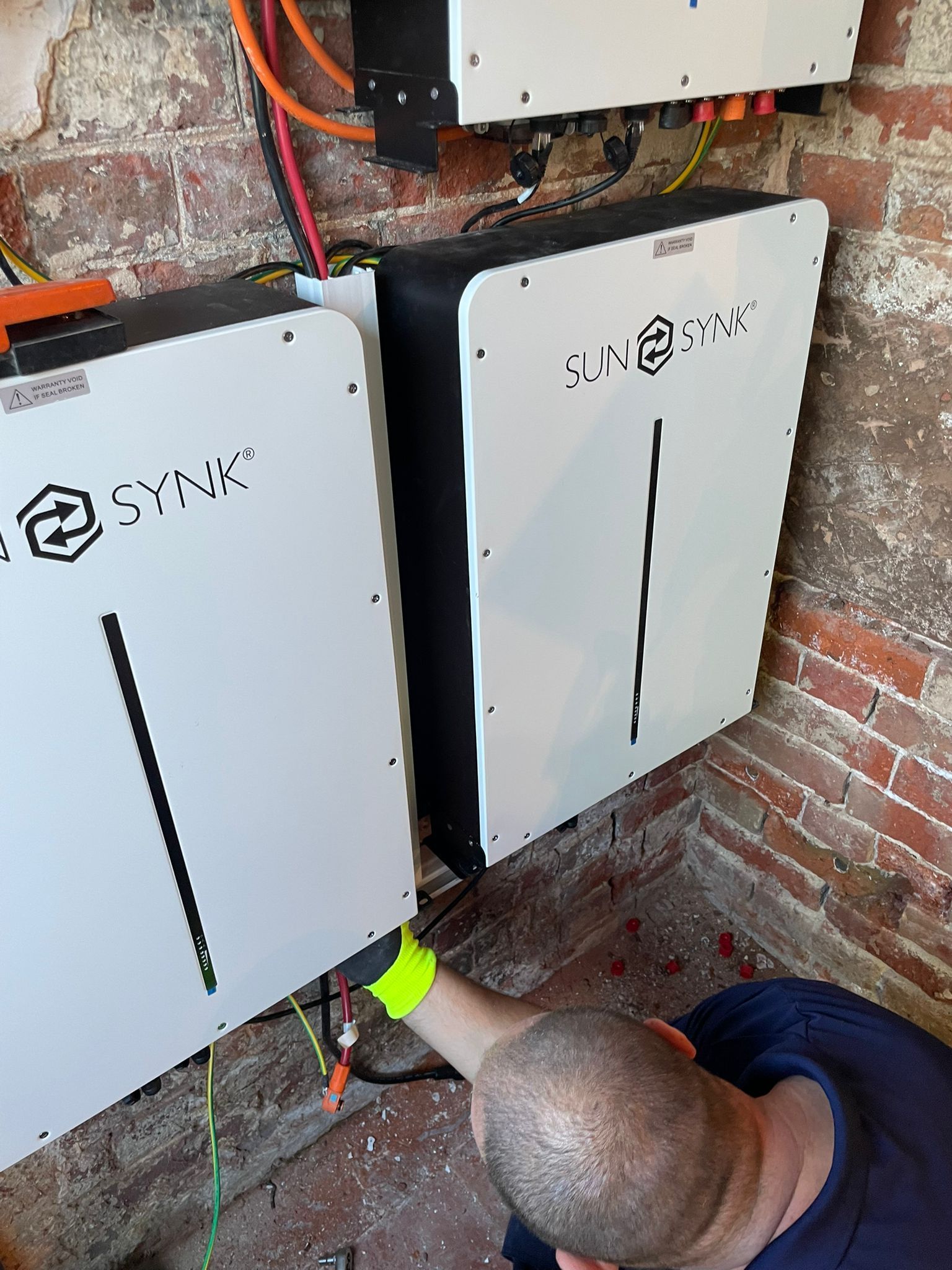 A person installs solar batteries on a brick wall. The batteries are white with black accents.