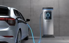 Silver electric car charging at a charging station in a garage. Blue cable connects the car and station.