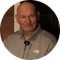 Bald man in gray jacket smiles; a small microphone hangs from his shirt.