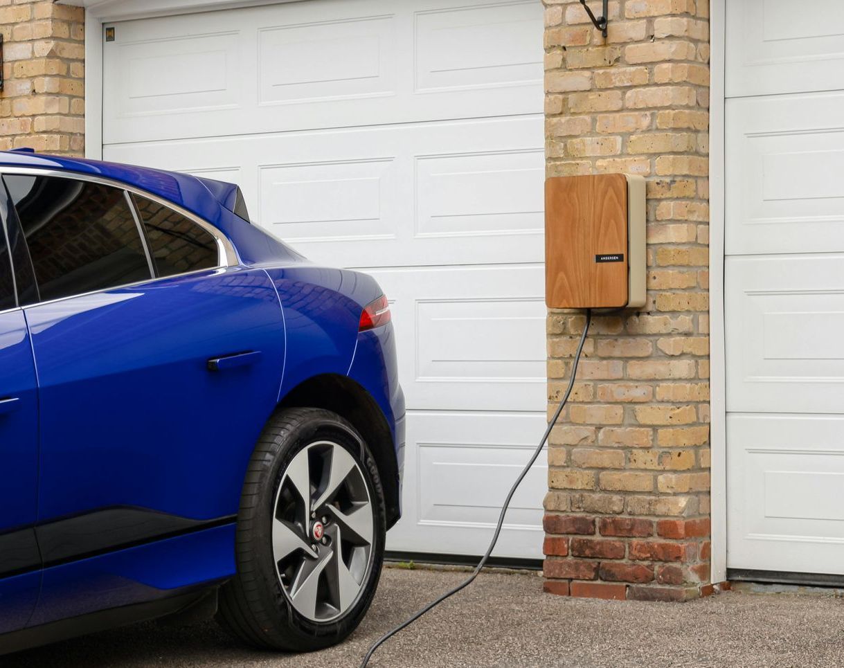 Blue electric car charging near a brick wall with a white garage door.