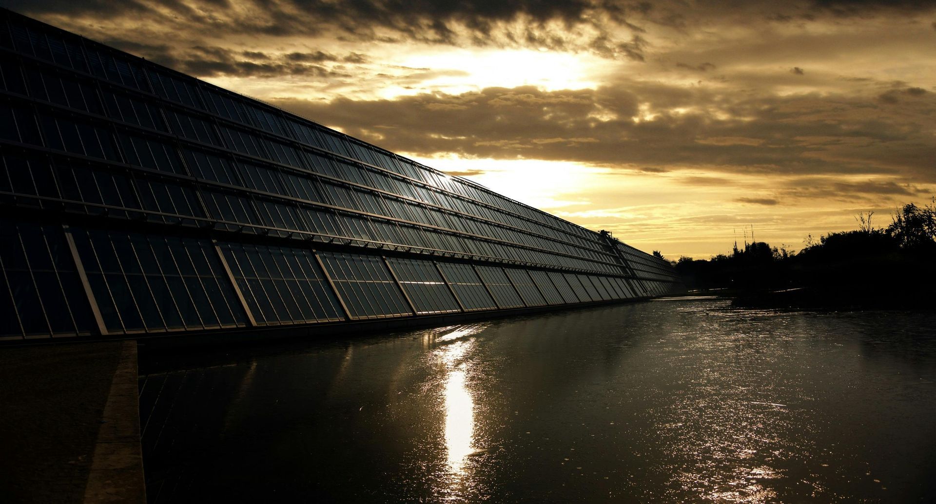 Solar panels over water reflecting sunset.