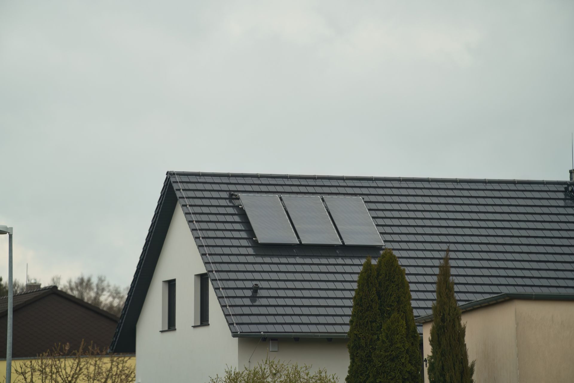 House with three solar panels on a gray tiled roof. Cloudy sky in the background.