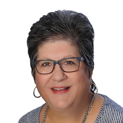Portrait of a smiling person with short dark hair, glasses, hoop earrings, and a striped top