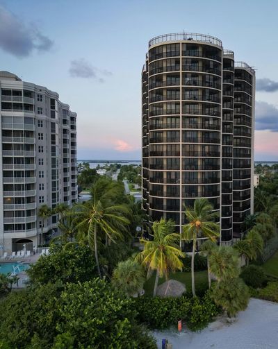 Two high-rise towers surrounded by palm trees at dusk, with a pink sky and a distant ocean view.