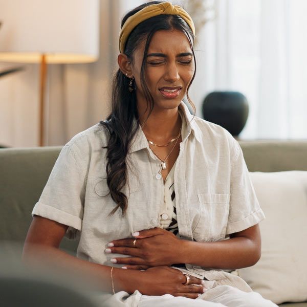 Woman sitting on a couch, eyes closed and holding her stomach in pain from severe bloating