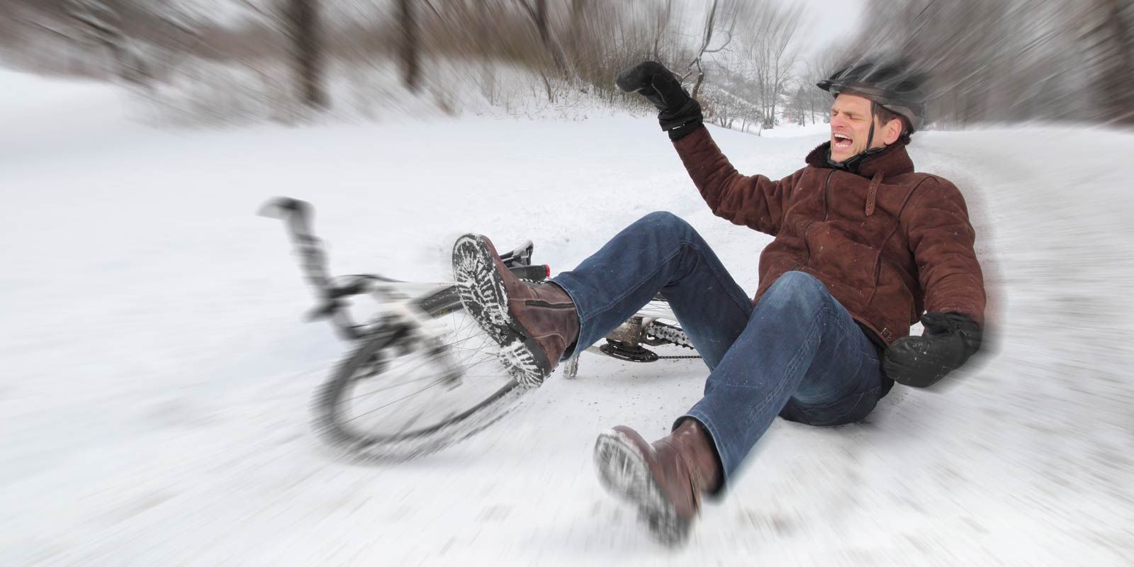 Man falls off bicycle on snowy ground, wearing a brown jacket, jeans, and a helmet, resulting in Coccydynia Treatments NYC by Dr. Alicia Armitstead