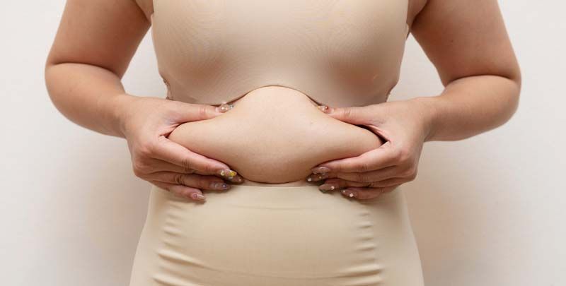 Person in nude body suit pinching excess belly fat considering collagen for weight loss