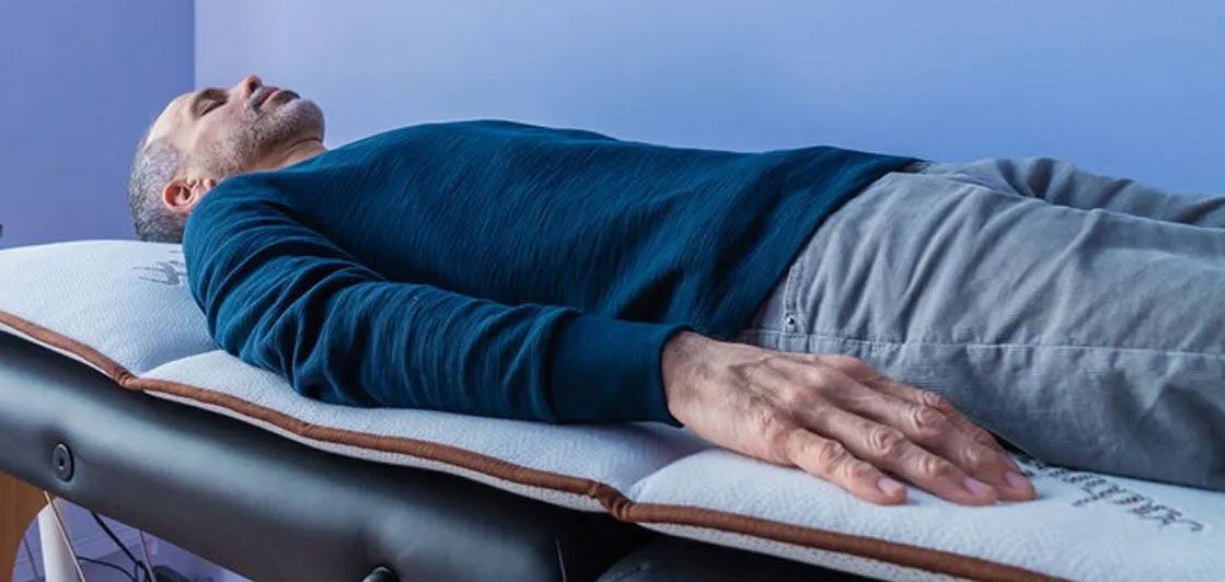 A man in a blue sweater is lying on a massage table getting PEMF Therapy for Detox, which starts with Voltage.