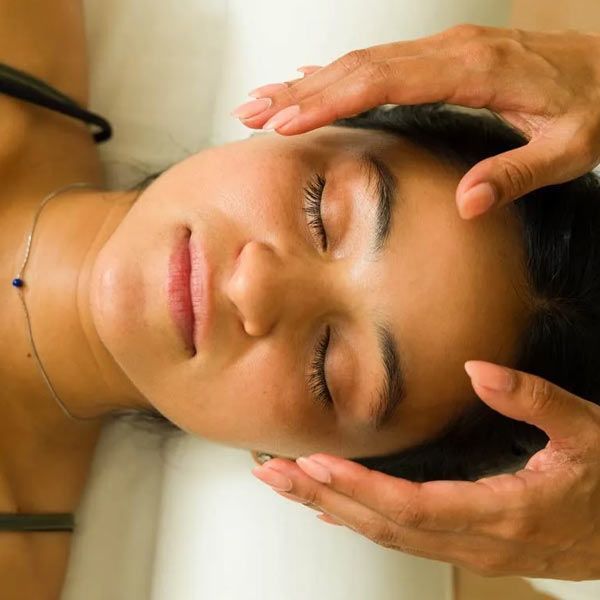 A person with closed eyes receiving a reiki treatment on their temples from another person's hands.