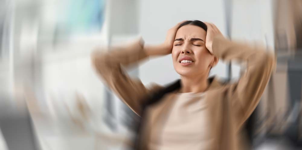 Woman with hands on head, eyes closed, experiencing stress, inside a blurred office setting. Hormone Imbalance and Stress