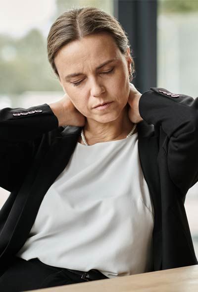 A woman in a suit is sitting at a table with her hands on her neck.