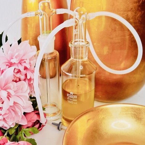 Nasal Insufflationn. Two glass bottles with tubes connected, filled with yellow liquid, set against gold decor and pink flowers.