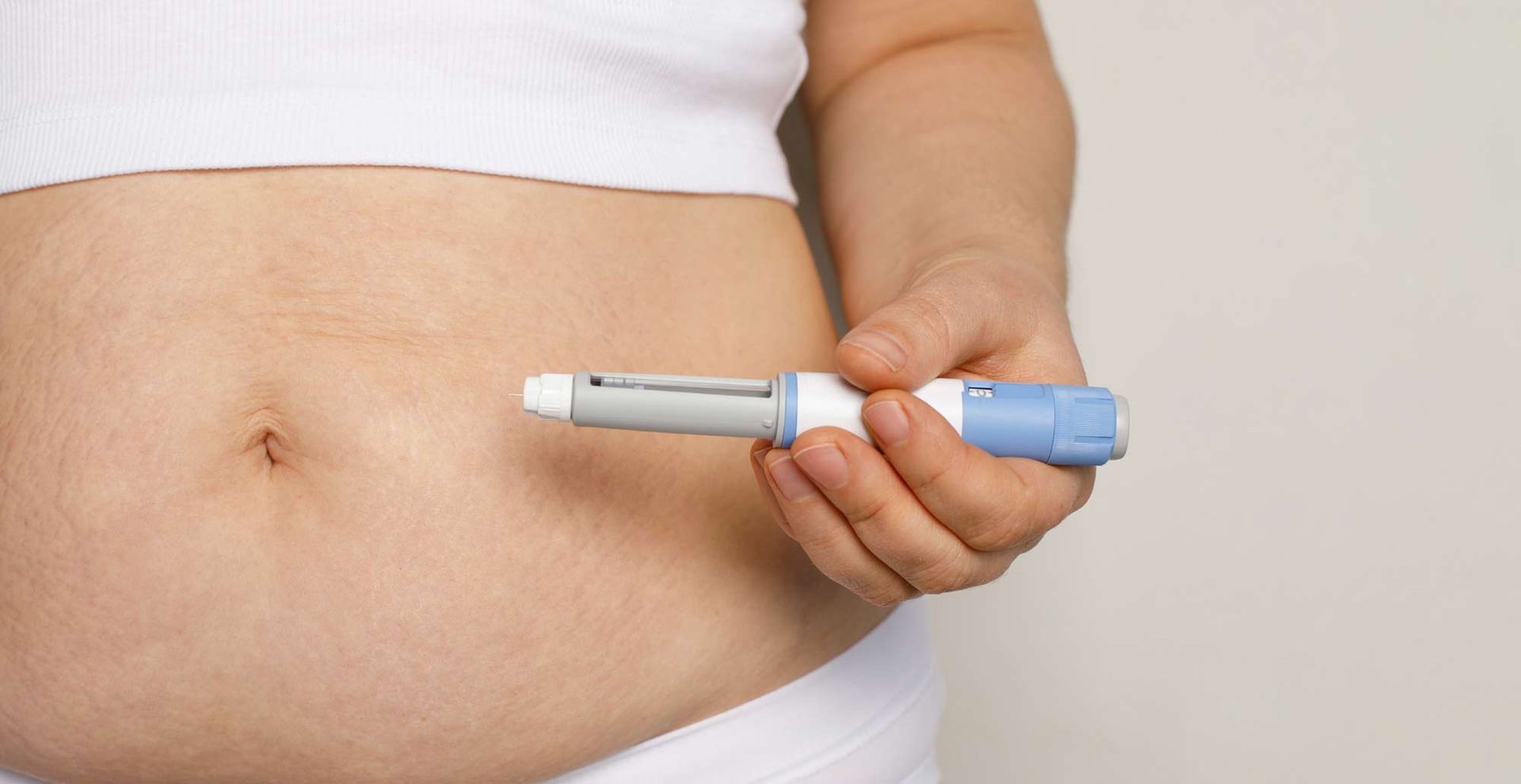 A woman is holding a syringe in front of her stomach considering Natural Alternatives to Ozempic