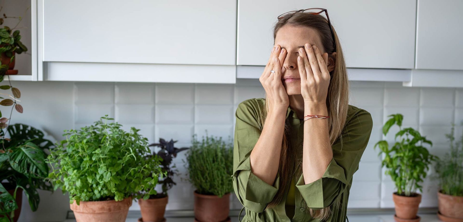 A woman is covering her eyes with her hands in a kitchen representing Premenstrual Dysphoric Disorder: Symptoms, Diagnosis, and Treatment