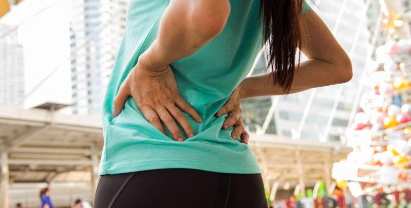 A woman in athletic wear holding her lower back, likely in pain, outdoors, experiencing the Warning Signs of Sciatica