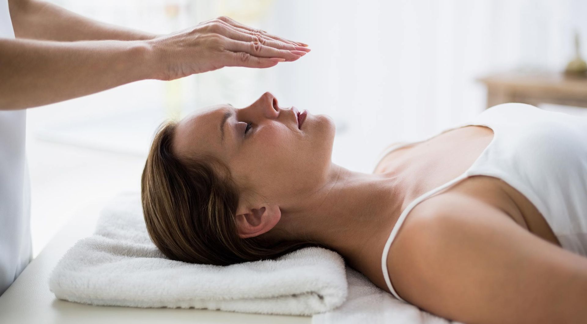 A woman is lying on a bed getting a Reiki healing treatment. Understanding Reiki and Its Impact on Well-Being