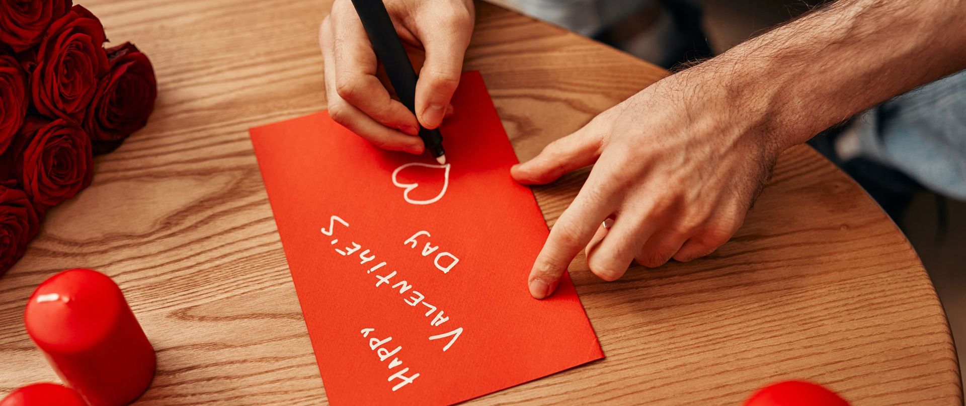 A man is writing a Valentine's Day card on a wooden table. A Valentine's Day Gift Poem for the Healing Arts NYC Spa Experience