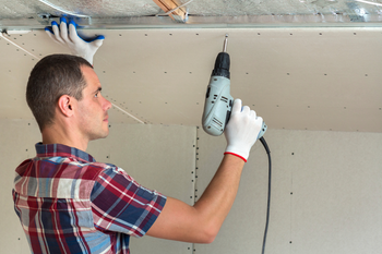 A man is using a drill to install a ceiling.