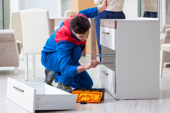 A man is working on a dresser in a living room.