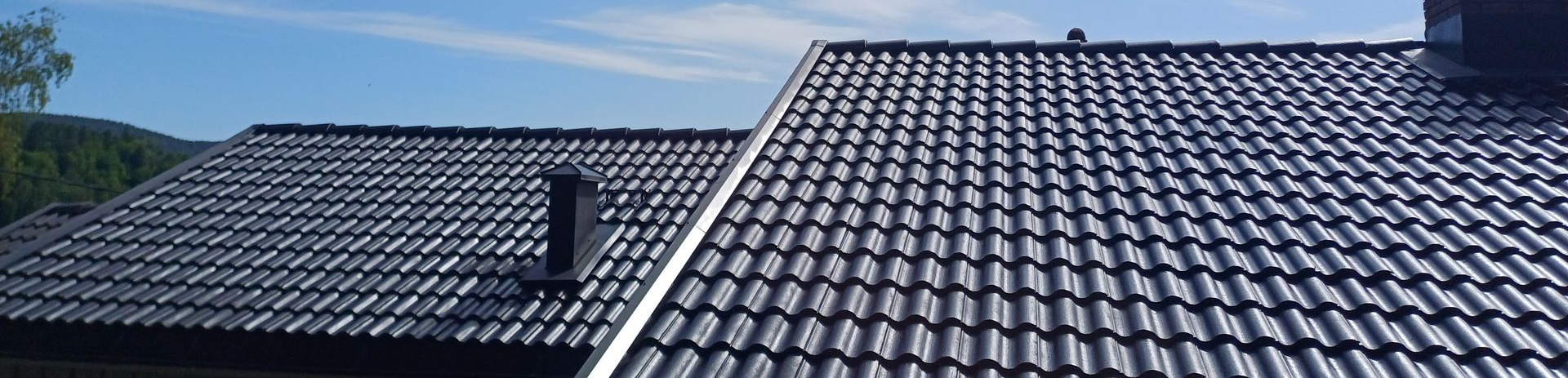 Et mørkt, teglsteinsbelagt skråtak under en blå himmel, med en skorstein