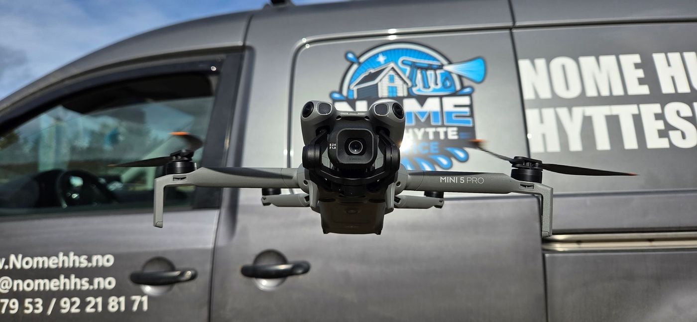 En hvit og svart DJI-drone som svever i luften mot en uskarp, lys bakgrunn.