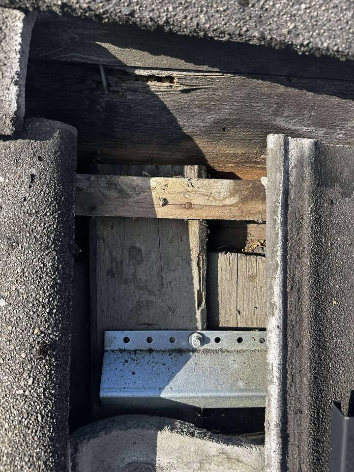Et nærbilde av en manglende takstein som avslører skadet undertak og et metallfeste festet til en sperre.
