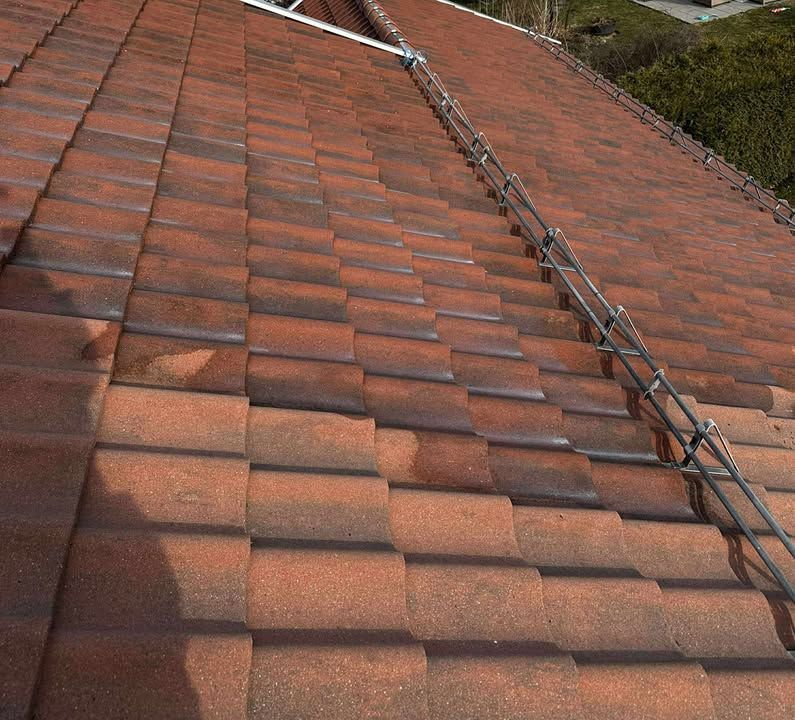 Et utsyn nedover en brun, flislagt takhelling med et metallrekkverk som går langs høyre kant.