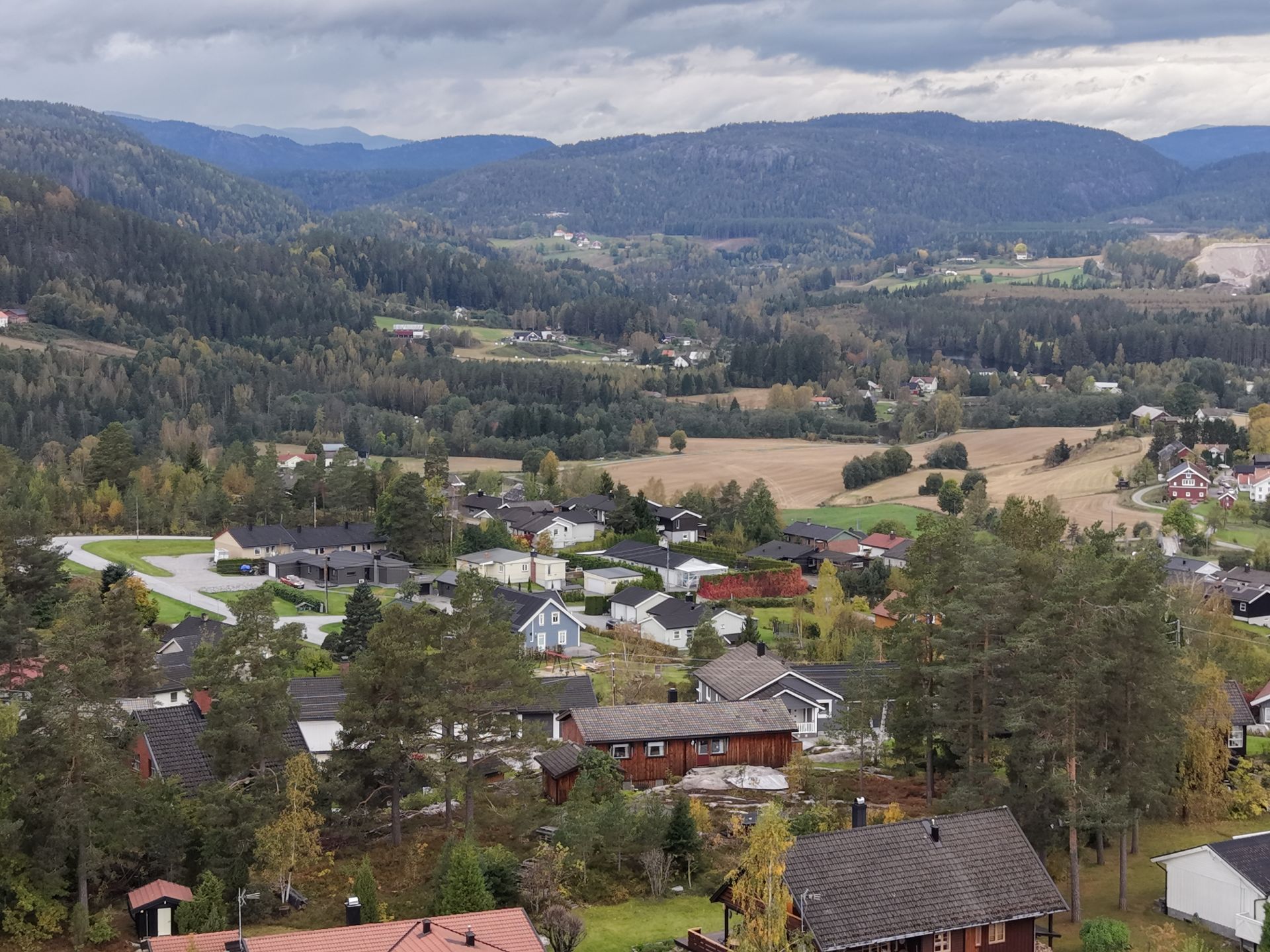 En naturskjønn utsikt fra høy vinkel over et boligstrøk som ligger i en dal omgitt av skogkledde åser og fjell.