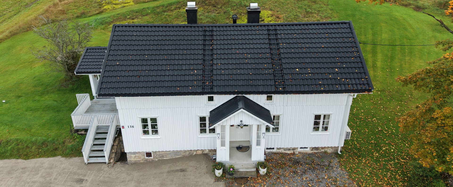 Luftfoto av et hvitt, enetasjes hus med svart tak, en liten veranda og tretrapper, omgitt av en grønn plen.