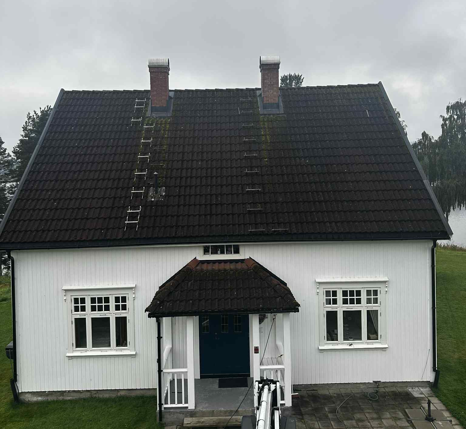 Et hvitt hus med vertikal trekledning, et mørkt tegltak, to skorsteiner og en liten gavlformet veranda.