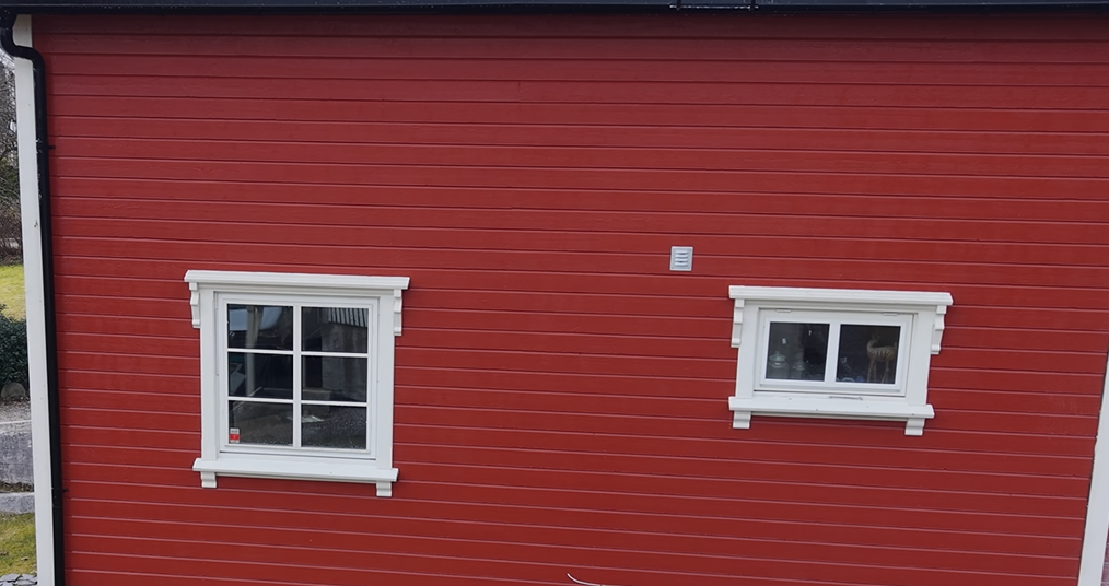 En rød trevegg med horisontal kledning, med to hvitinnrammede vinduer i forskjellige størrelser og dekorative listverk.