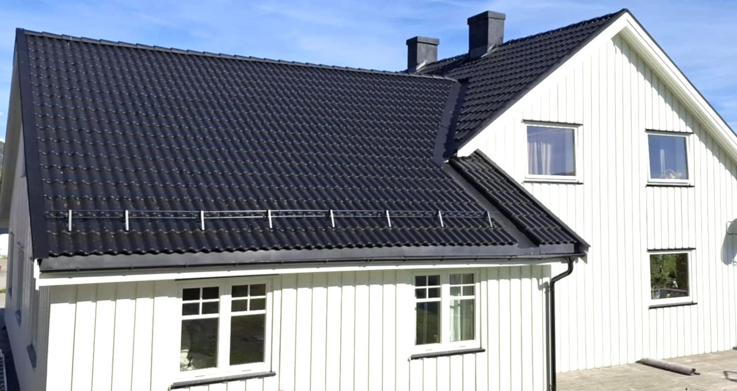 Et hvitt hus med mørkt saltak og vertikal trekledning under en blå himmel.