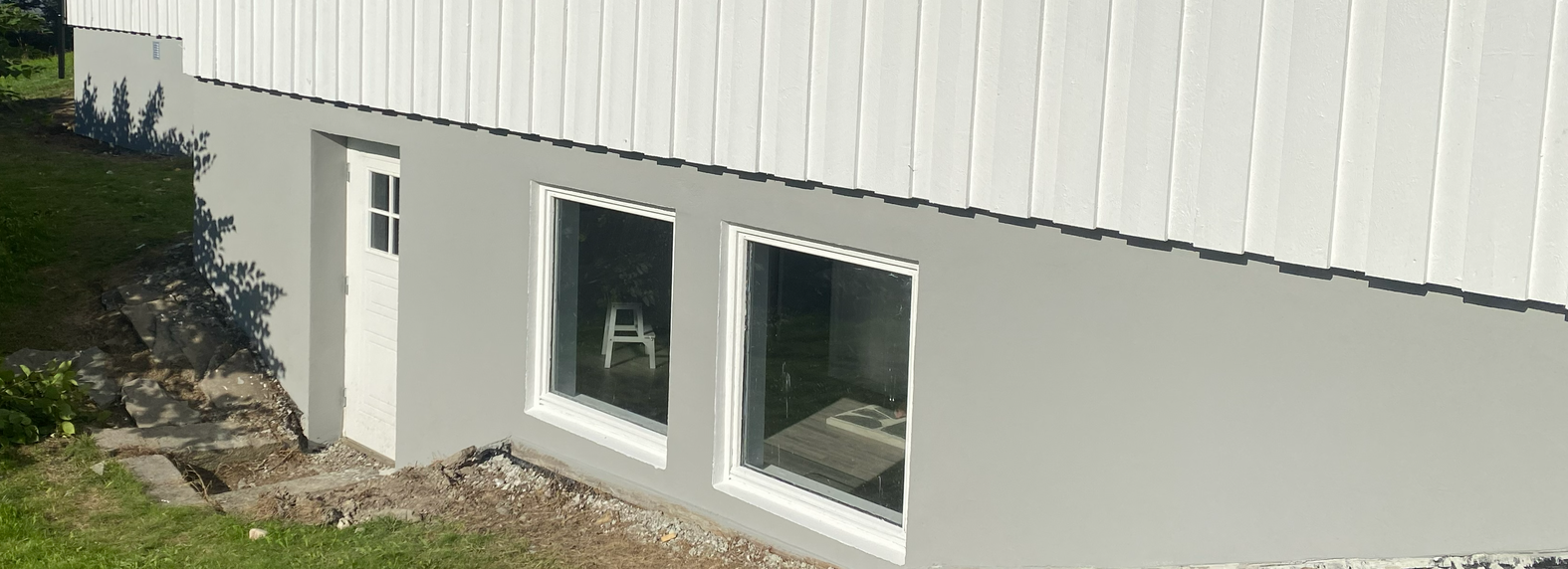 En bygning med hvite sider og et grått betongfundament, med en liten hvit dør og to rektangulære vinduer.