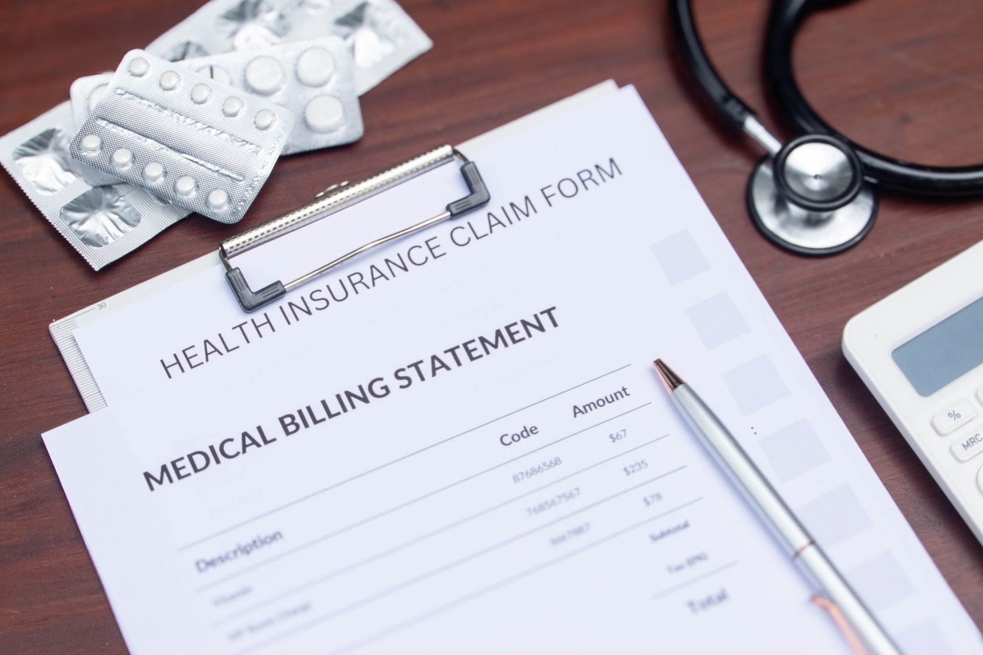 Health insurance claim and medical billing forms with pills, pen, stethoscope, and calculator on a desk