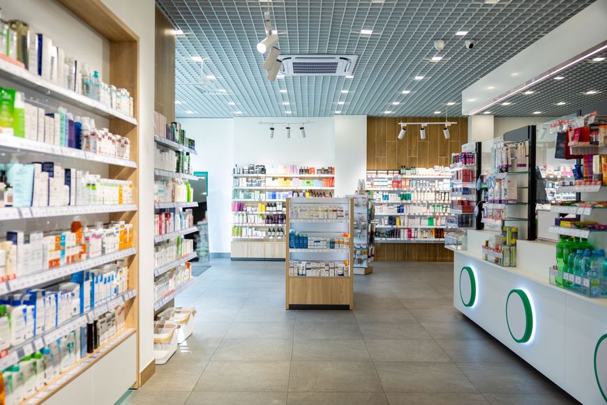 Bright, modern pharmacy aisle with shelves of medicines and a white counter in the foreground