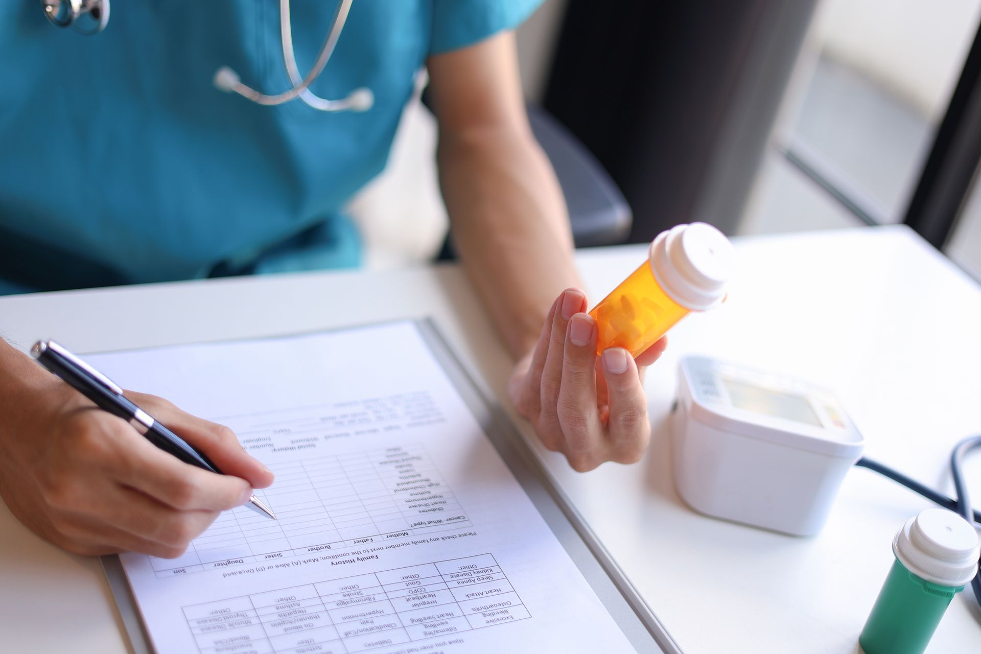 Person writing on a medical form while holding an orange pill bottle beside a white container.