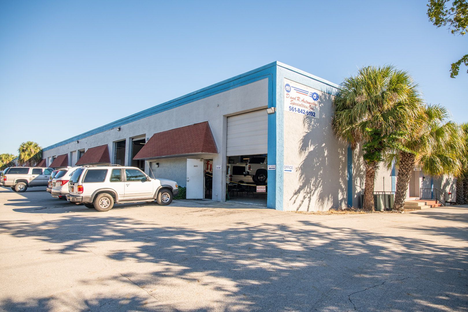 Auto repair shop with several bays, vehicles parked outside, palm trees.