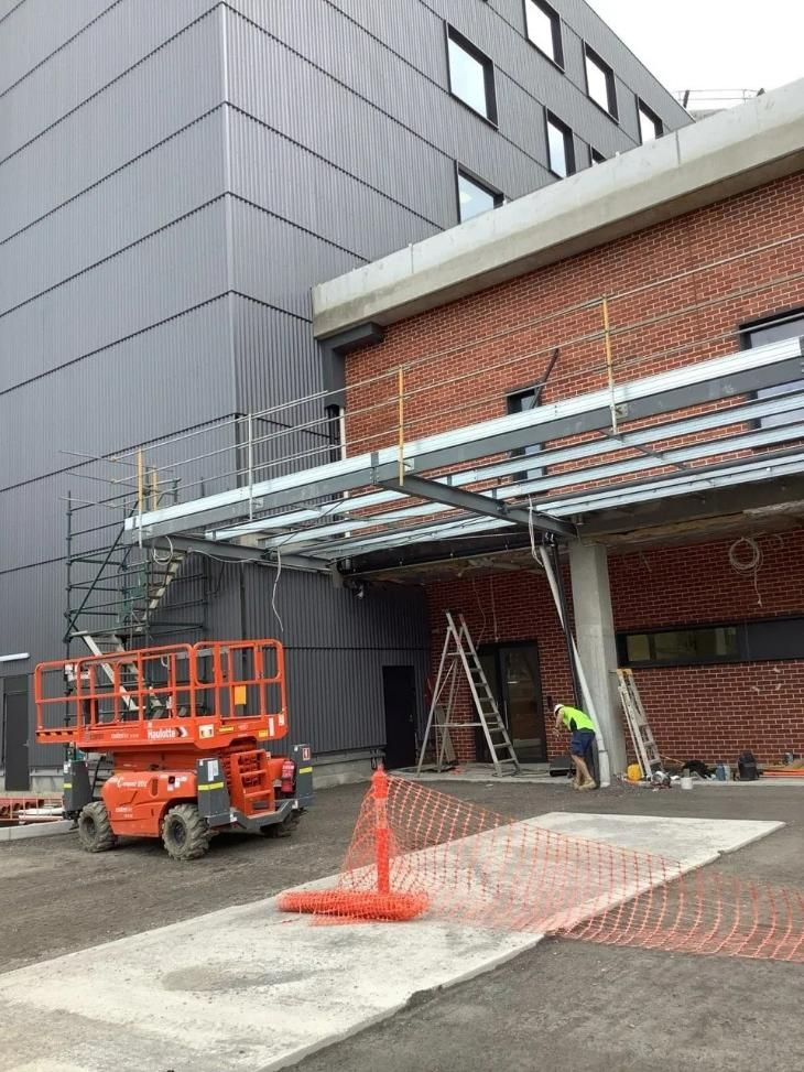 A Construction Vehicle Is Parked in Front of A Large Building — Site Safety NSW in Sandgate, NSW